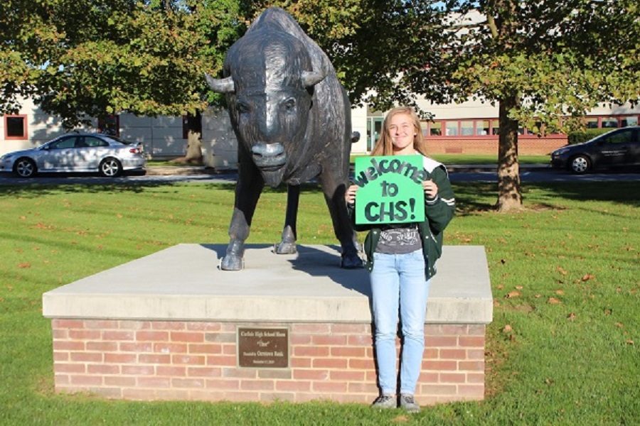 Carol Etzel holds a welcome sign in front of the McGowan entrance. Carlisle High School is offering a new group as a way to help new students transition to the school.