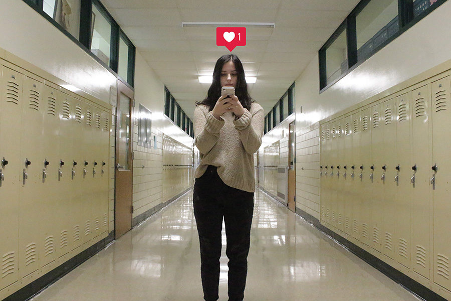 A student stands in a hallway staring at her phone, looking over Instagram. 
