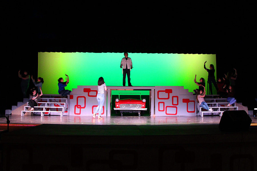 The cast poses around the stage to rehearse a scene with the entrance of the red car.