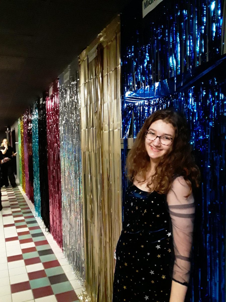 ERAS: Sophie Haque, freshman, stands in front of a wall of streamers color-coded for each Taylor Swift era