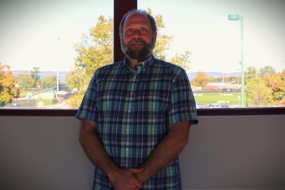 Mr. Sollman poses in front of a window on the walking bridge connecting Swartz and Fowler