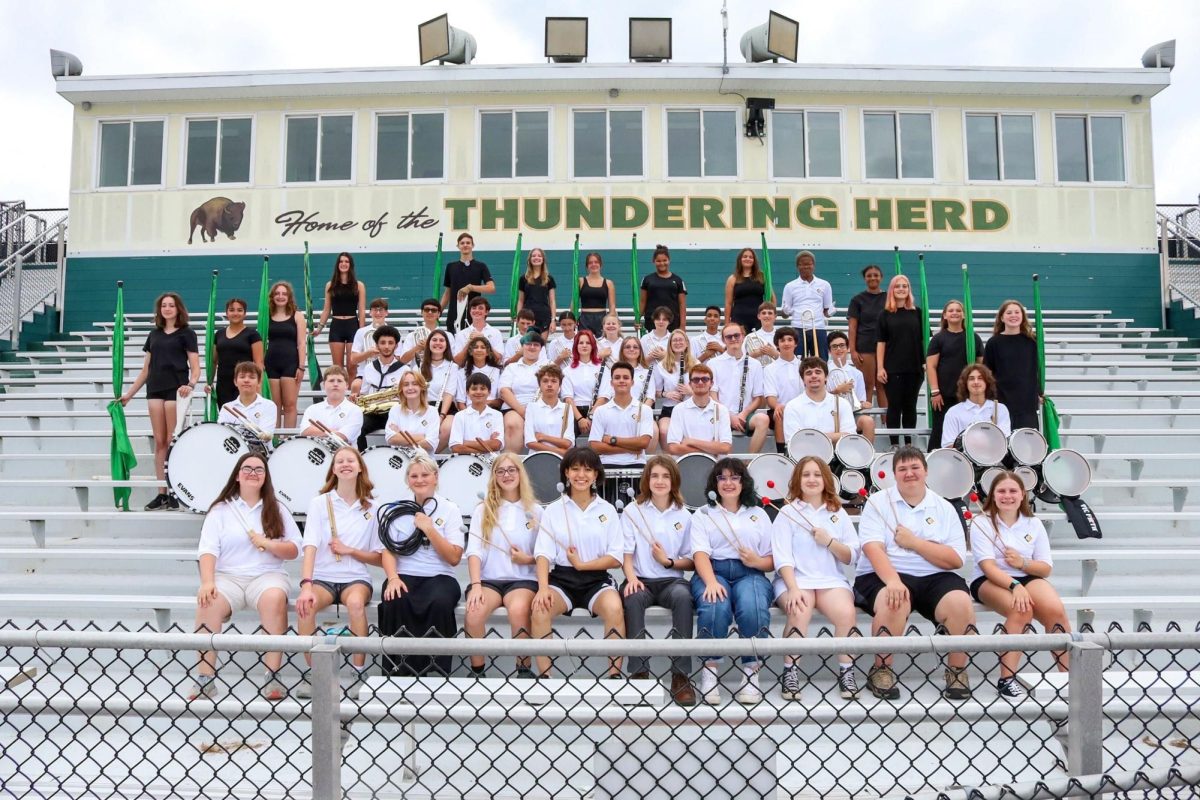 The marching band stands along the bleachers for a team photo.