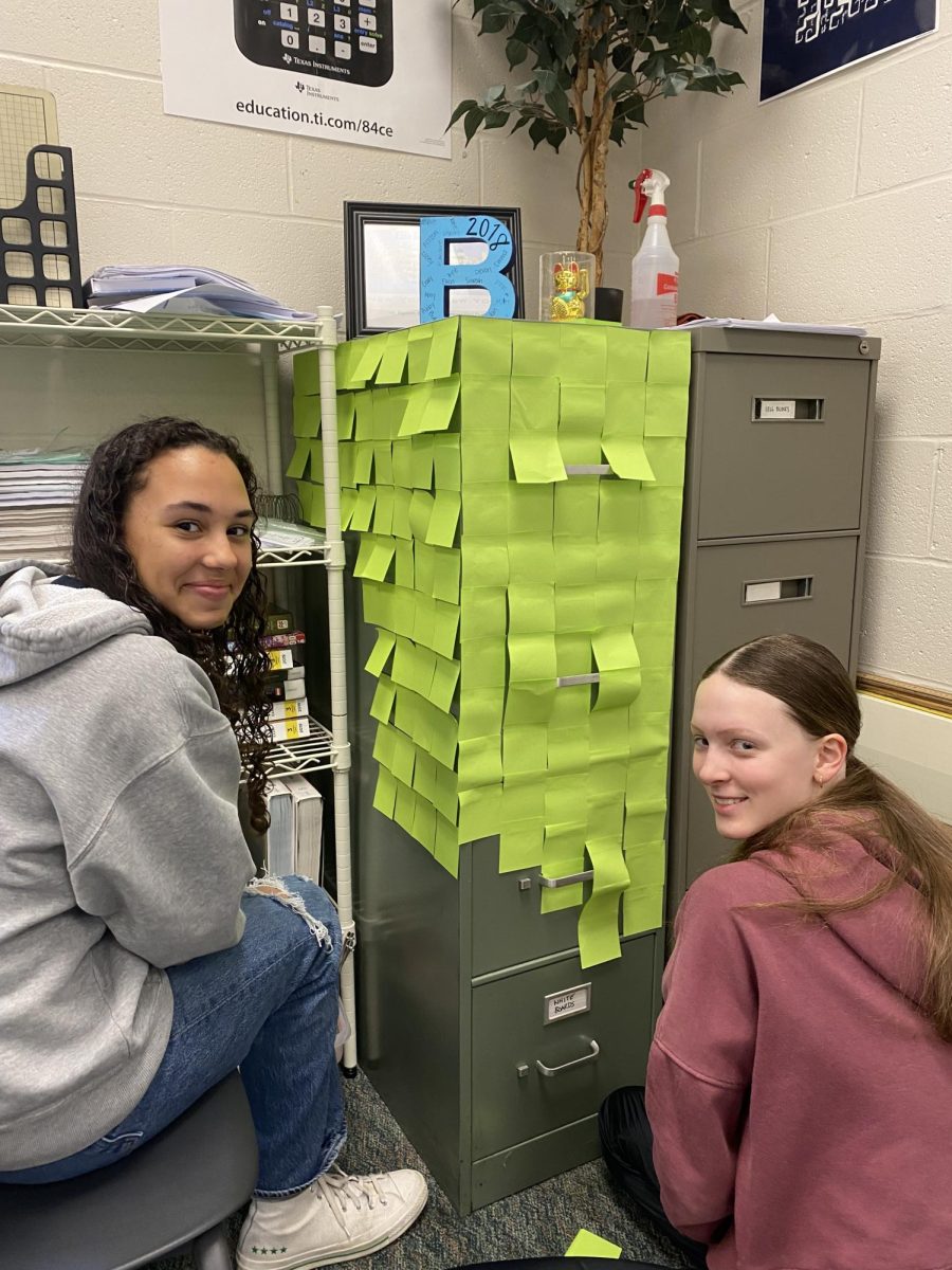 Felonica Kirkham and Alison Negley work in part of the team to cover the front section of the room, the whiteboard, smartboard, and filing cabinets in green sticky notes.