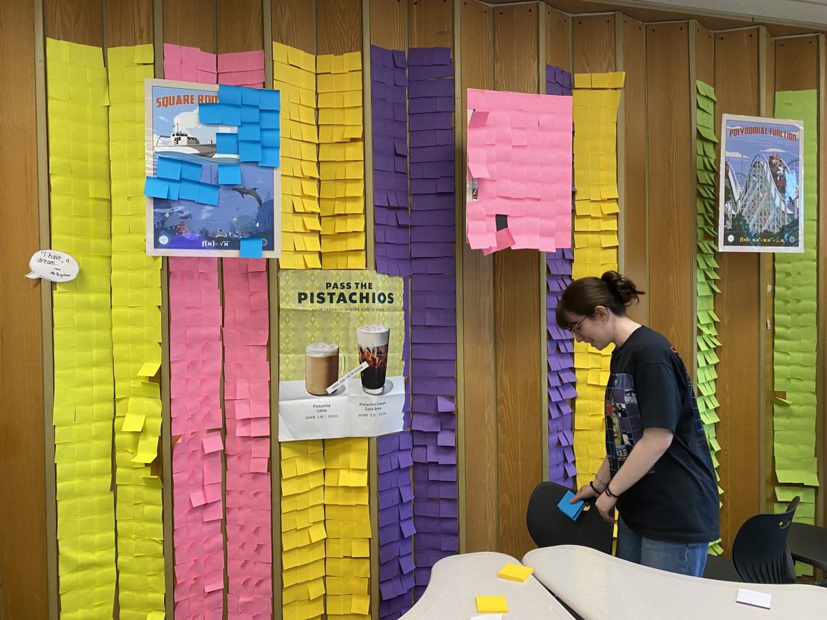Sarah Forrester works with a group of over ten people to sticky note the back wall divider, in different color stripes of sticky notes. 